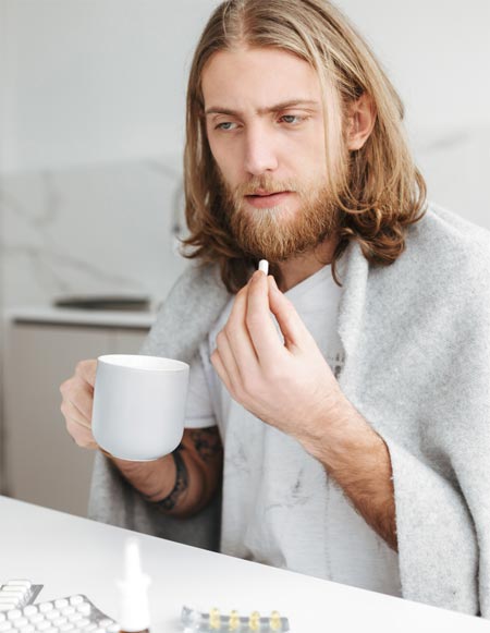 ill man sitting with mug and pills in hands in kit DF5X3J8